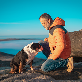 Man kneeling down with dog on hillside